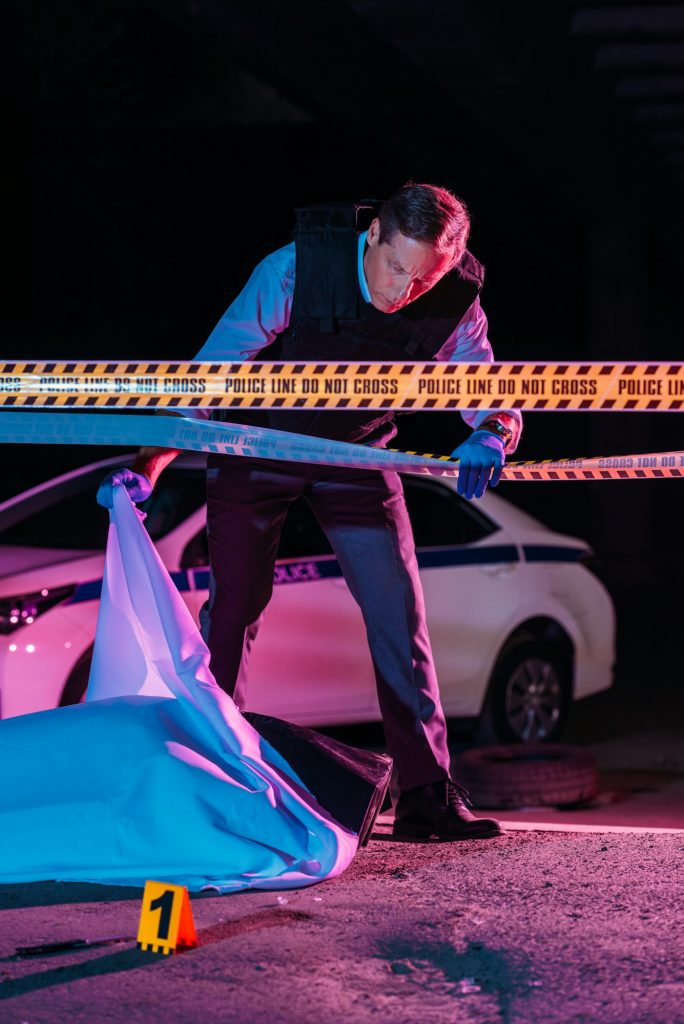 middle aged male police officer looking at corpse in body bag at crime scene