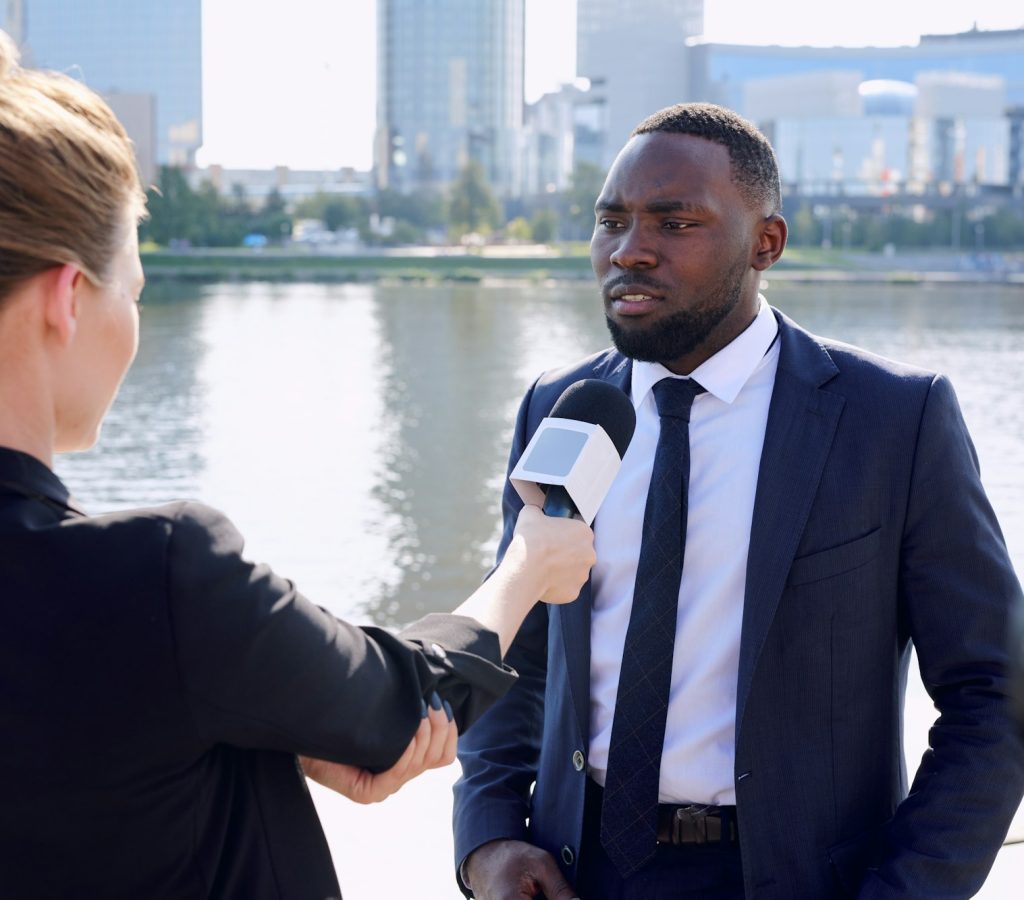 Young African entrepreneur standing in front of female reporter or journalist with microphone